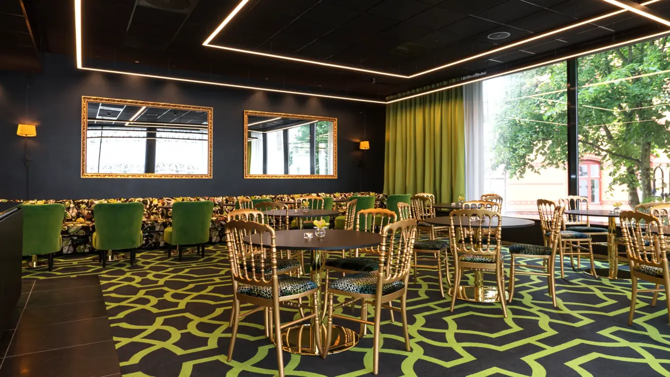 Lounge med mønstret gulvteppe i svart og grønt, gullfargede stoler, lenestoler i forskjellige farger og store vinduer på Thon Hotel Stavanger midt i Stavanger sentrum