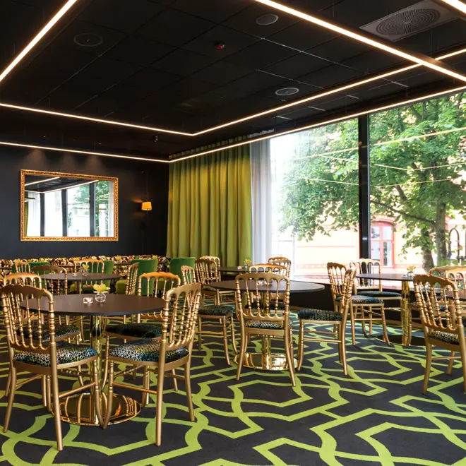 Lounge med mønstret gulvteppe i svart og grønt, gullfargede stoler, lenestoler i forskjellige farger og store vinduer på Thon Hotel Stavanger midt i Stavanger sentrum