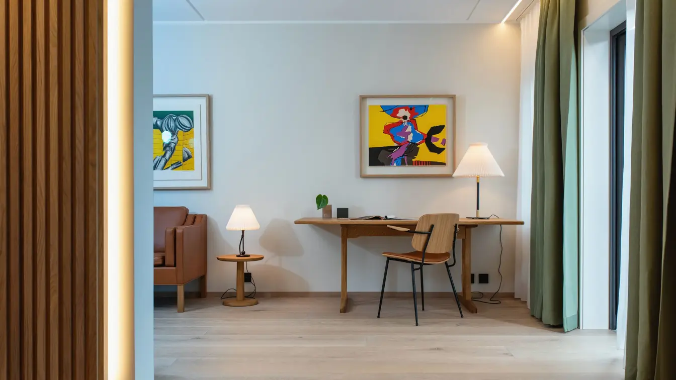 Skrivebord og stol i træ, med leselampe. Stort vindu med grønne gardiner.  I suite på Thon Hotel Norge i Kristiansand.