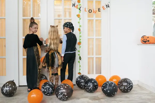 Rear view of Caucasian children in pretty Halloween costumes standing on porch, knocking on the door and asking for treats