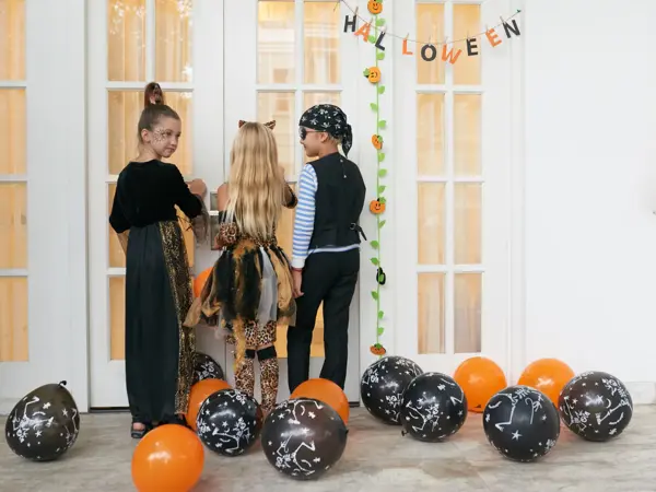 Rear view of Caucasian children in pretty Halloween costumes standing on porch, knocking on the door and asking for treats