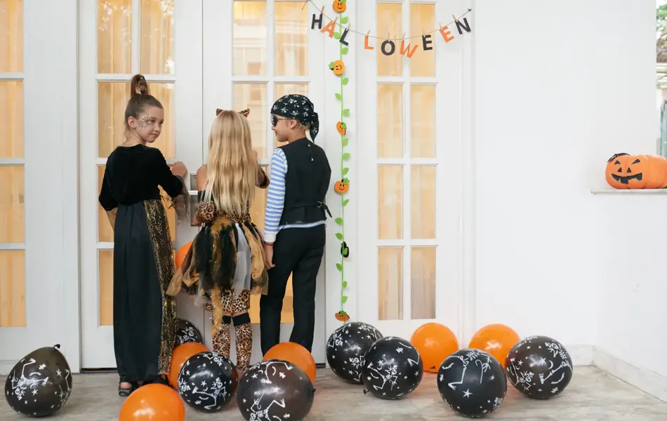 Rear view of Caucasian children in pretty Halloween costumes standing on porch, knocking on the door and asking for treats