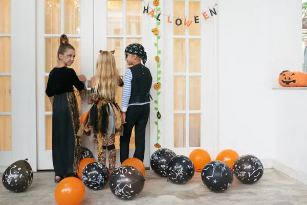 Rear view of Caucasian children in pretty Halloween costumes standing on porch, knocking on the door and asking for treats