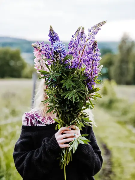 Jente som holder stor lilla og grønn bukett foran ansiktet 