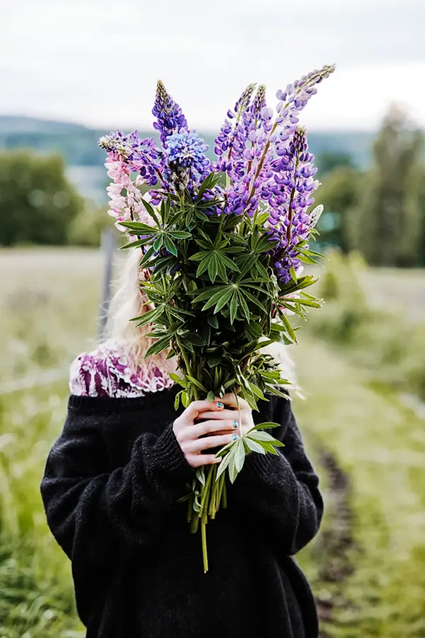 Jente som holder stor lilla og grønn bukett foran ansiktet 