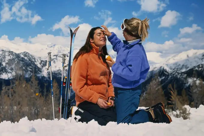 Dame som smører en venninne med solkrem i ansiktet ute i naturen