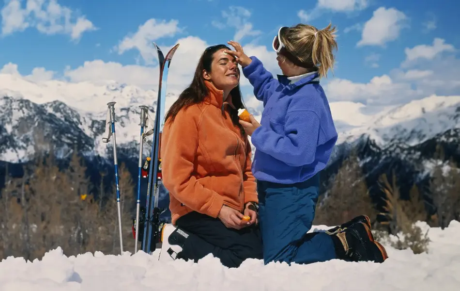 Dame som smører en venninne med solkrem i ansiktet ute i naturen