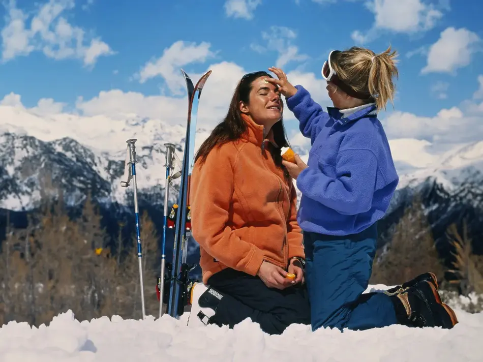 Dame som smører en venninne med solkrem i ansiktet ute i naturen