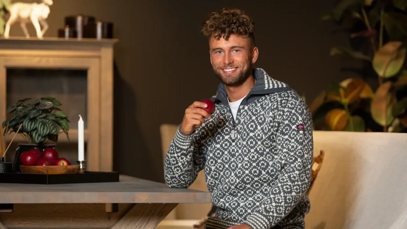 Smilende mann i strikkegenser holder eple