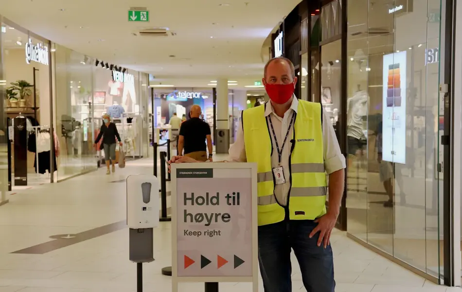 Bilde av mann med munnbind ved plakat i kjøpesenter
