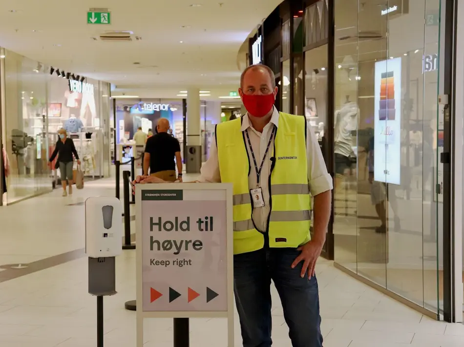 Bilde av mann med munnbind ved plakat i kjøpesenter