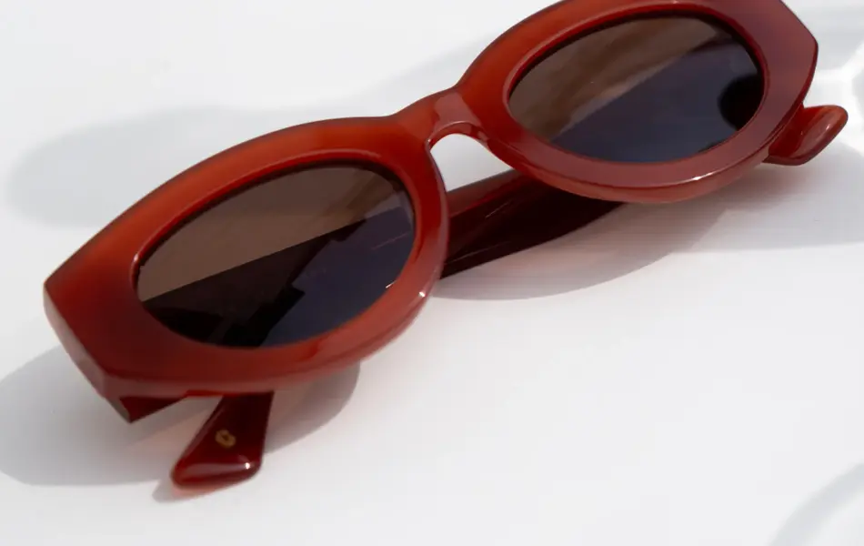 Rødbrune solbriller med tykk innramming på et bord.