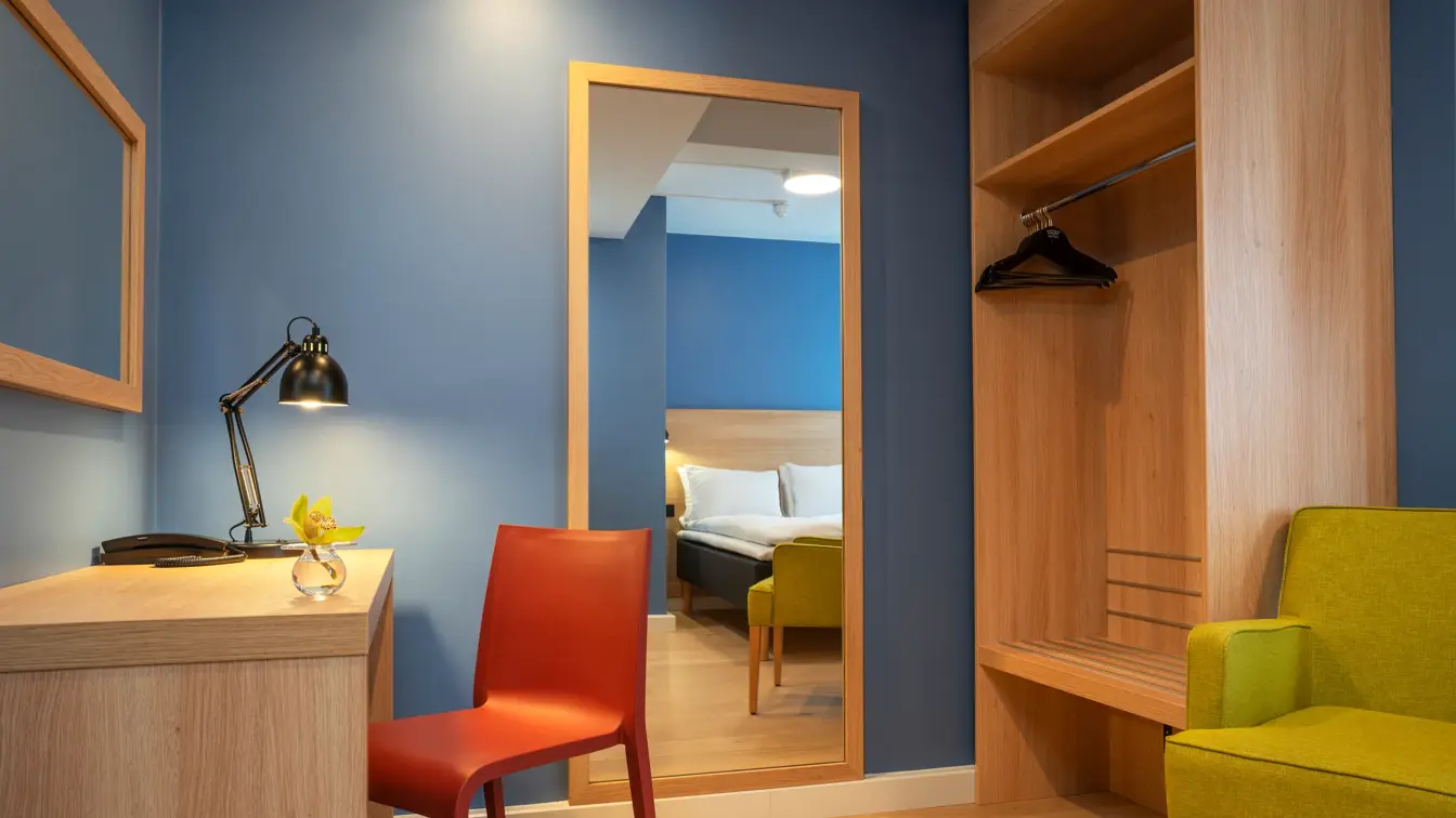 Skrivebord, speil, blå vegger, garderobe og gul stol i standard rom queen på Thon Hotel Astoria