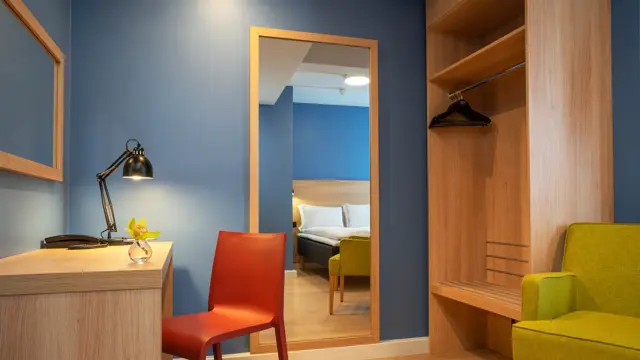 Skrivebord, speil, blå vegger, garderobe og gul stol i standard rom queen på Thon Hotel Astoria