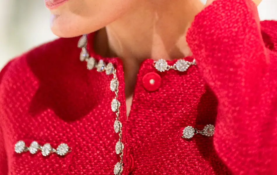 Dame med sort sløyfe i håret, øredrobber med stener, rød jakke med strassdekor.
