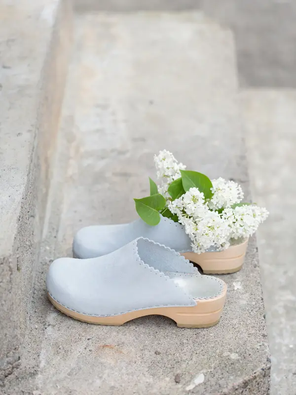 Nærbilde av lysegrå tresko som står på murtrapp med hvite blomster i