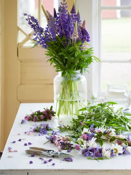 Blomsterbukett i lilla og grønt arrangeres på bord 