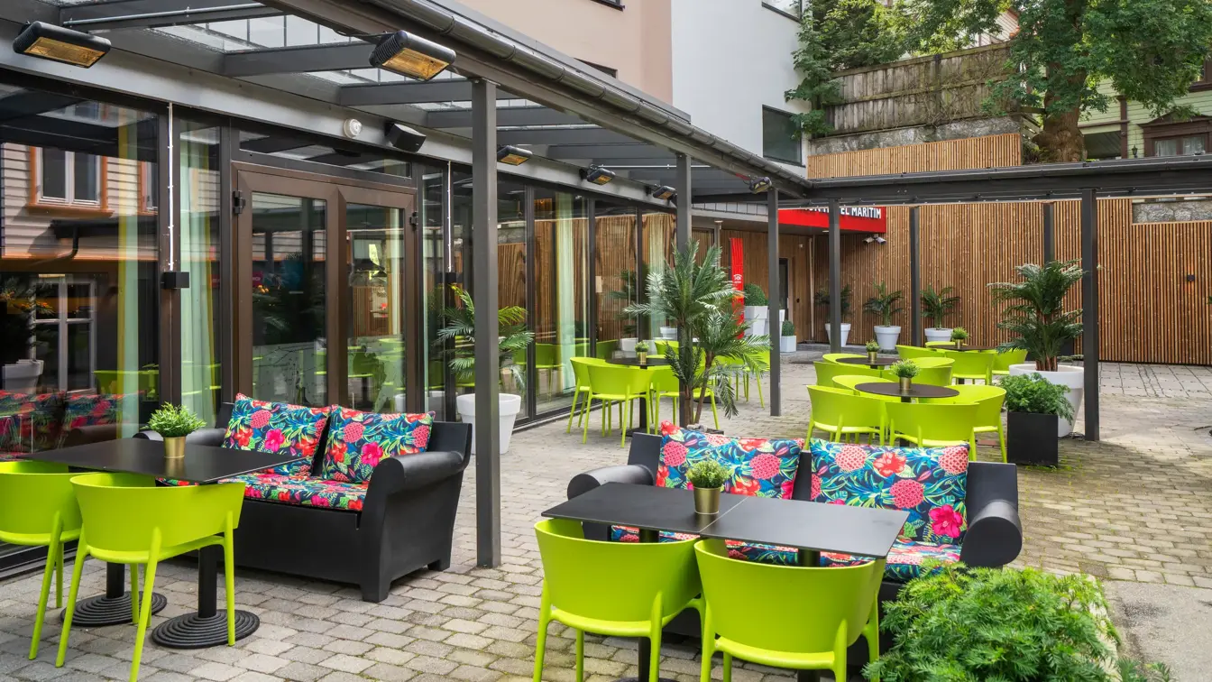 Sittegrupper med grønne stoler, fargerike blomstrete sofaer og sorte bord på uteområde utenfor Thon Hotel Maritim