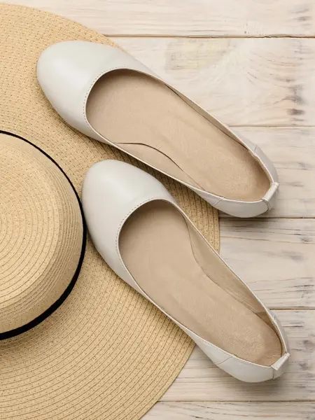 Et par hvite ballerinasko som ligger ved siden av en strå hatt