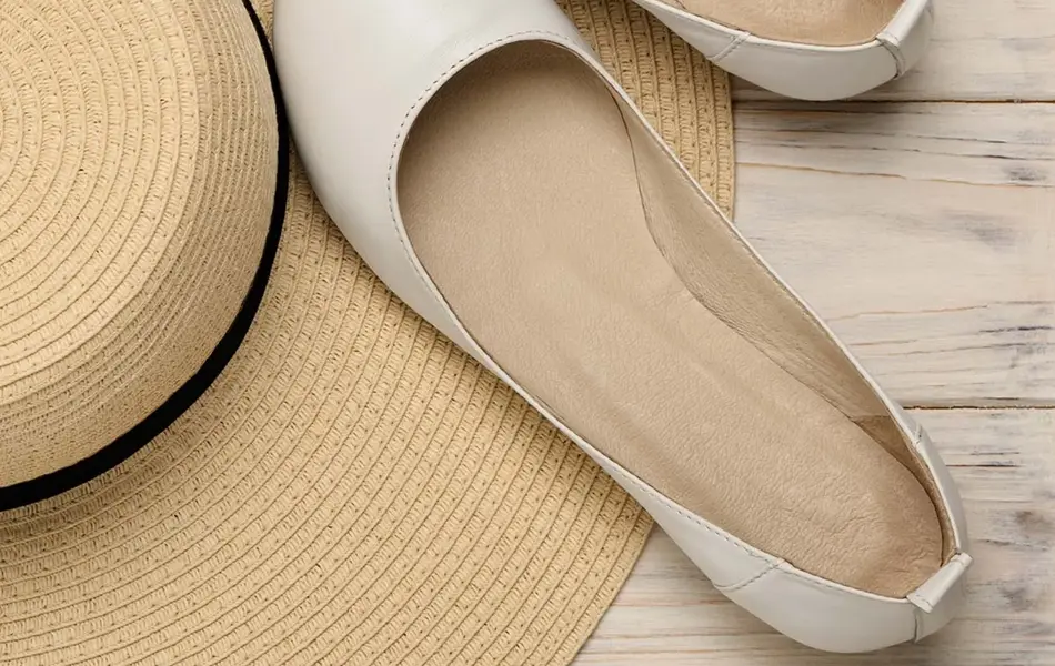 Et par hvite ballerinasko som ligger ved siden av en strå hatt