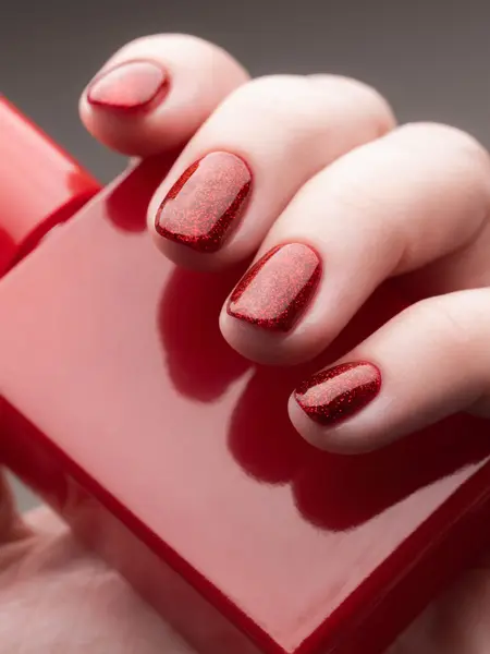 Nærbilde av hånd med rød neglelakk som holder en rød neglelakkflaske