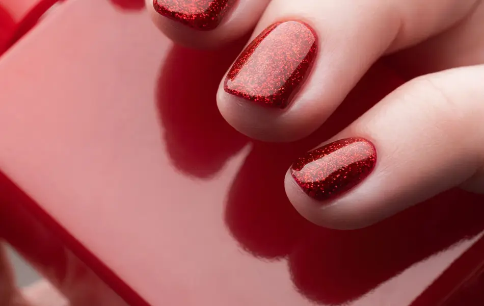 Nærbilde av hånd med rød neglelakk som holder en rød neglelakkflaske