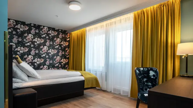 Skrivebord, parkettgulv, skrivebord, stol, dobbeltseng, vindu, gule gardiner, blomstertapetvegg