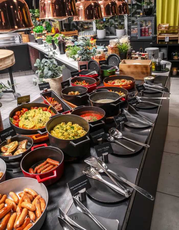 Frokostbuffet med diverse varmmat i svarte og røde kjeler.