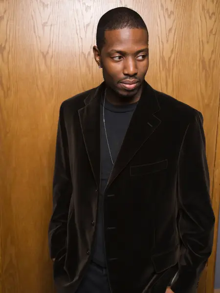 Mann med sort fløyelsjakke poserer foran trevegg 