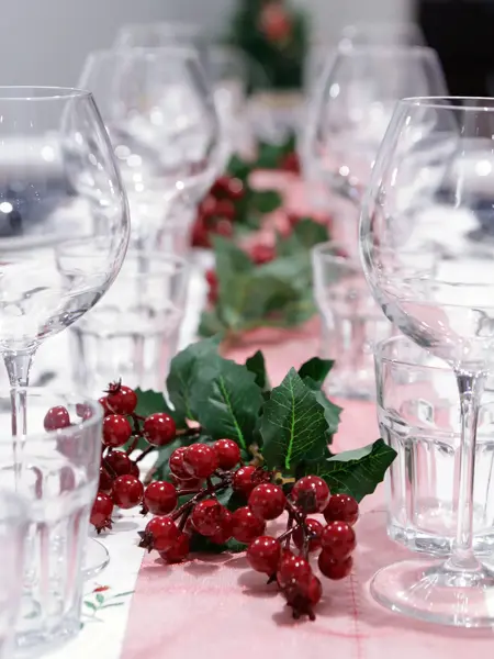 Nærbilde av langbord som er pyntet med glass, rød løper og røde bær. Foto til artikkel om bryllupsmenyer tilpasset sesong.