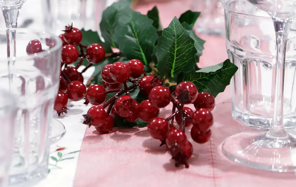 Nærbilde av langbord som er pyntet med glass, rød løper og røde bær. Foto til artikkel om bryllupsmenyer tilpasset sesong.