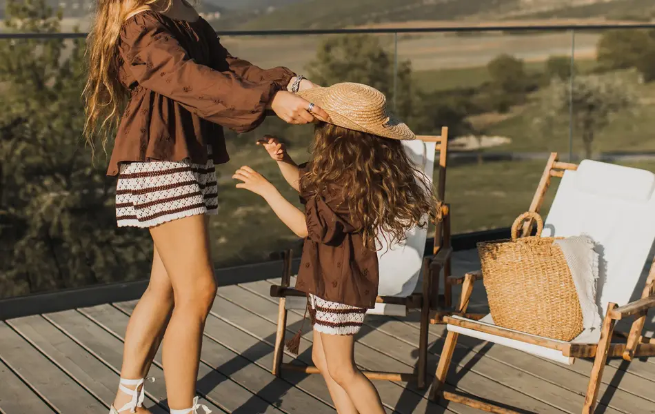 Dame med brun skjorte, stripete shorts og sandaler leker med datter i matchende antrekk 