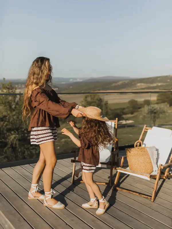 Dame med brun skjorte, stripete shorts og sandaler leker med datter i matchende antrekk 
