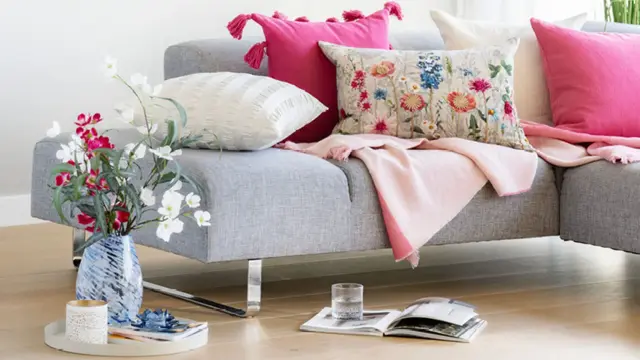 Grå sofa med fargerike puter, vase med blomster og en bok på gulvet