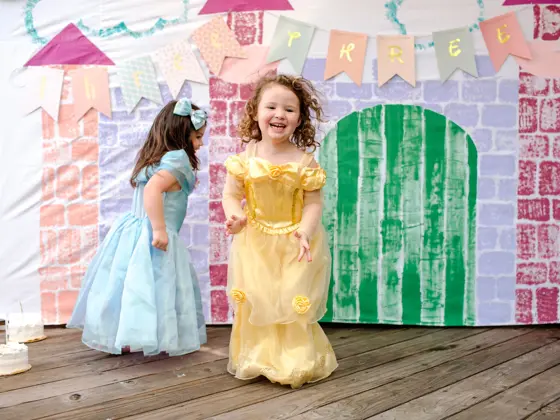 To jenter kledd ut som prinsesser hopper foran et lateslott