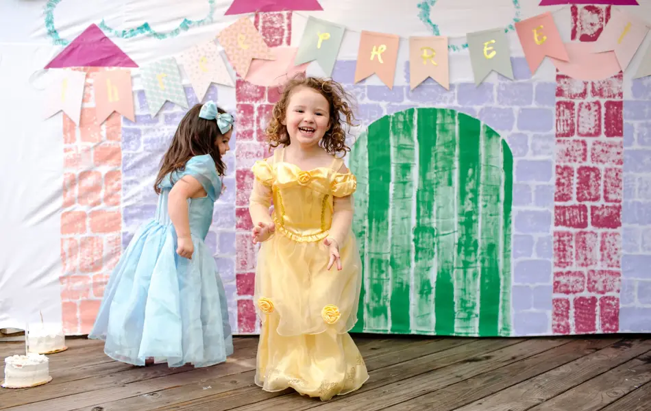 To jenter kledd ut som prinsesser hopper foran et lateslott