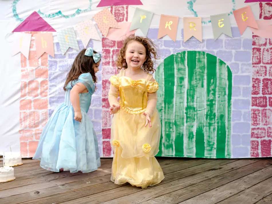 To jenter kledd ut som prinsesser hopper foran et lateslott