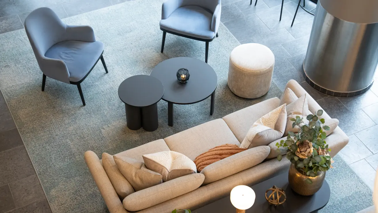 Beige sofa, sofabord og blå lenestoler i lobby sett ovenifra.