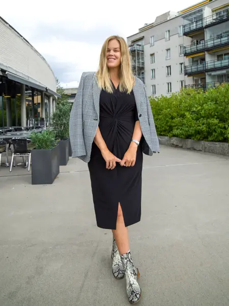 Jente med blondt hår, har på seg en lang sort kjole med en gråsort blazer over skuldrene