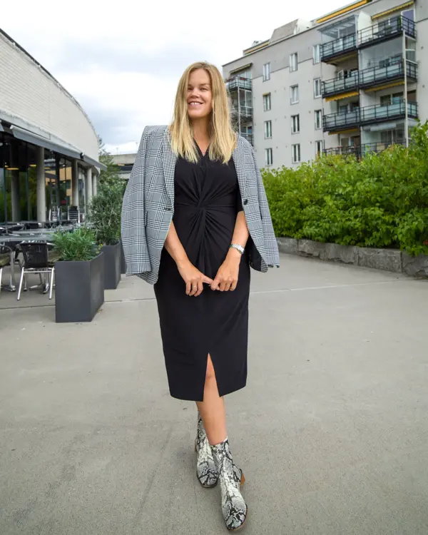 Jente med blondt hår, har på seg en lang sort kjole med en gråsort blazer over skuldrene