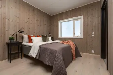Bildet viser visningsleilighet på Høyfjellstunet på Skeikampen. Soverommet har trepanel på veggen, stort garderobeskap i mørk brun. Sengen er oppredd med fargerike puter, grått sengeteppe og et oransje pledd.