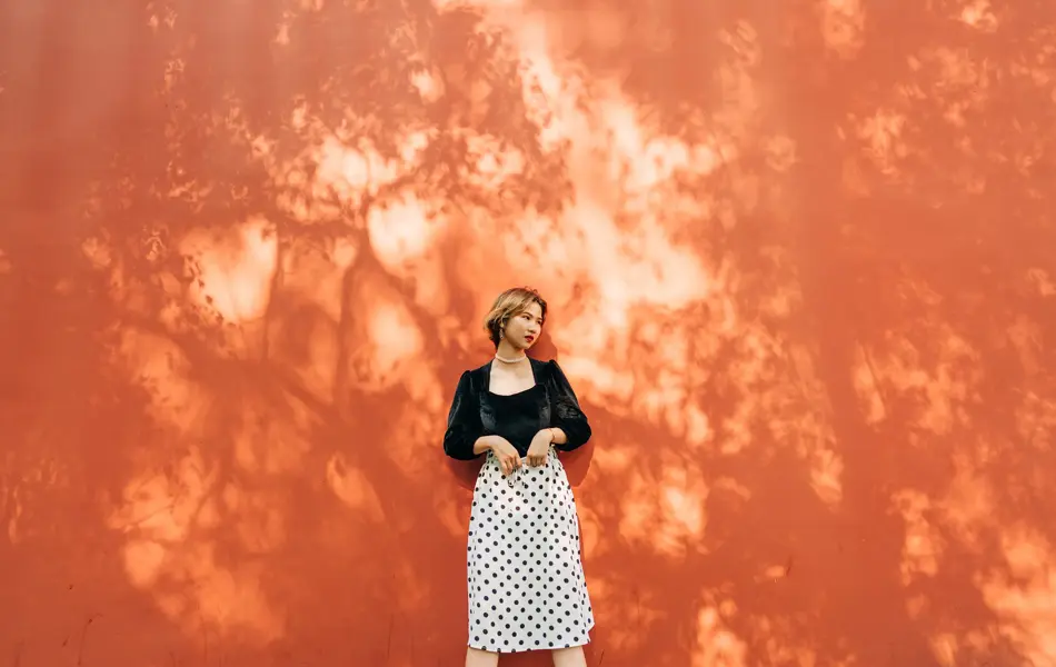 Dame med sort fløyelstopp og hvitt polkadotskjørt står inntil oransje vegg 
