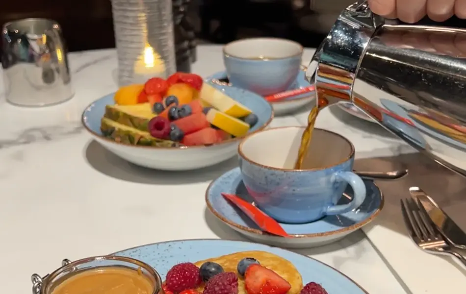 Noen som heller kaffe i en kopp og servise med frokost