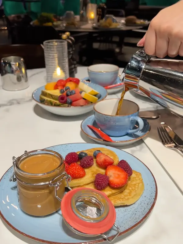 Noen som heller kaffe i en kopp og servise med frokost