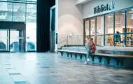 Jente leser en bok utenfor biblioteket ved inngangspartiet til Vestkanten Storsenter
