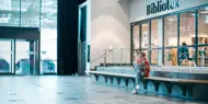 Jente leser en bok utenfor biblioteket ved inngangspartiet til Vestkanten Storsenter
