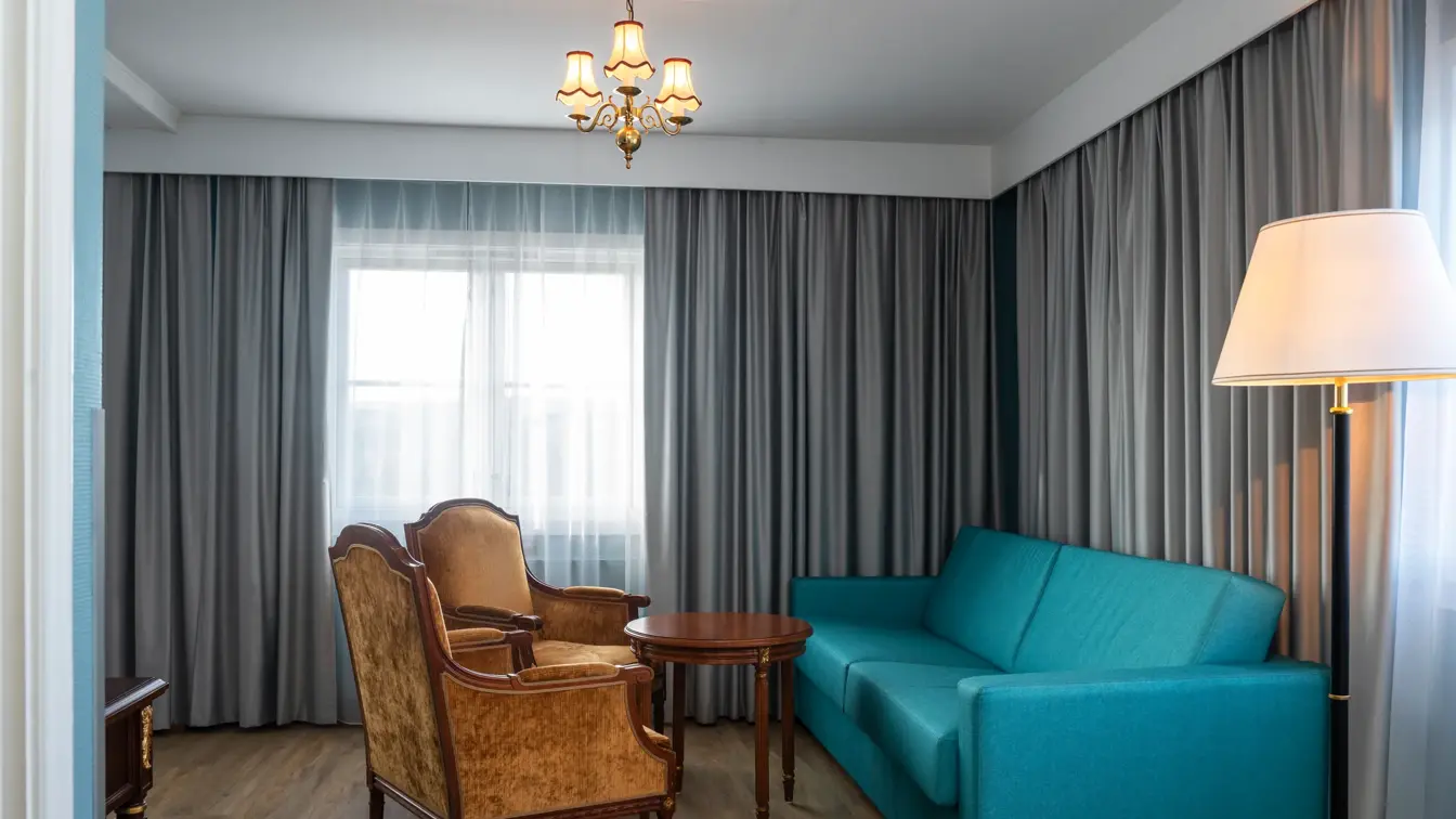 Blå sofa, salongbord, to sitte stoler, parkettgulv, grå gardiner. 