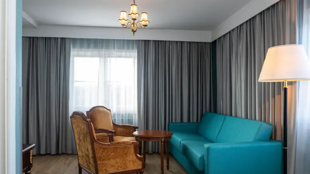 Blå sofa, salongbord, to sitte stoler, parkettgulv, grå gardiner. 