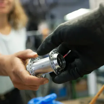 A close up of a technician handing her colleague a bike part while working together in a bicycle workshop.