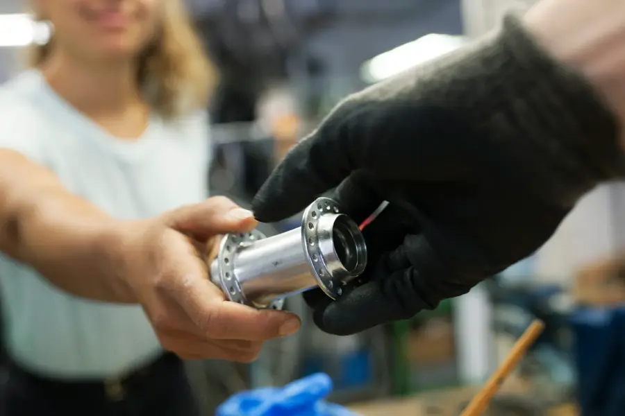 A close up of a technician handing her colleague a bike part while working together in a bicycle workshop.
